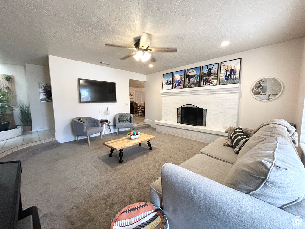 Carpeted living area featuring a ceiling fan, baseboards, a fireplace, a textured ceiling, and recessed lighting