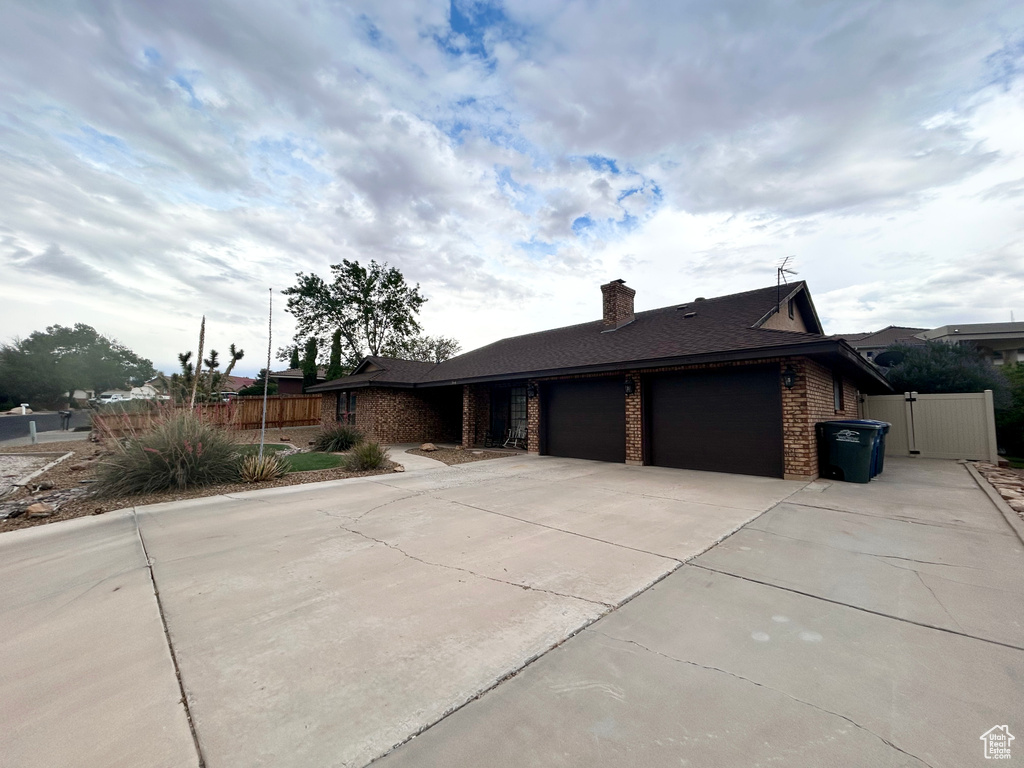 View of front of house featuring an attached garage, brick siding, concrete driveway, a gate, and a chimney