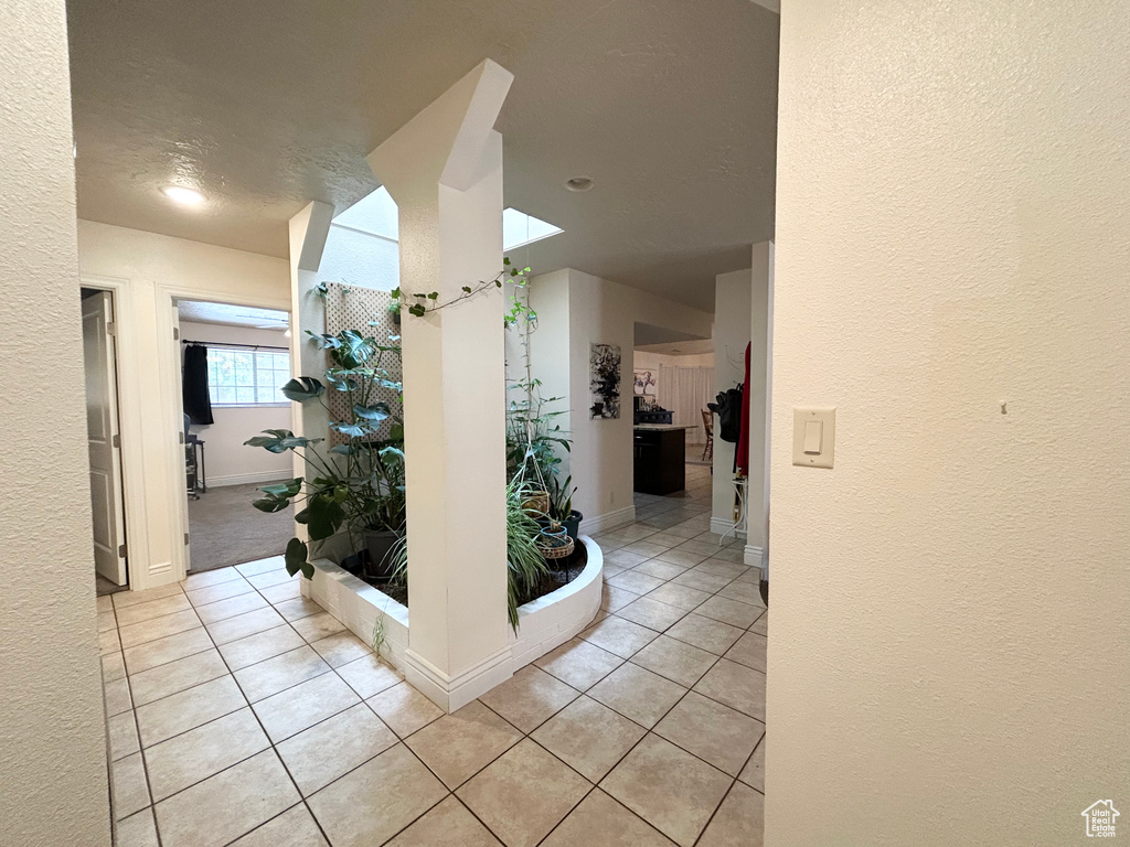 Hallway with a textured wall, light tile patterned floors, and baseboards