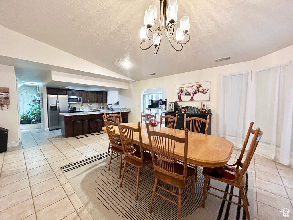 Dining room featuring light tile patterned floors, a chandelier, vaulted ceiling, a textured ceiling, and arched walkways