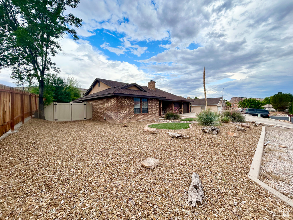 View of property exterior featuring brick siding, a gate, an attached garage, and a chimney