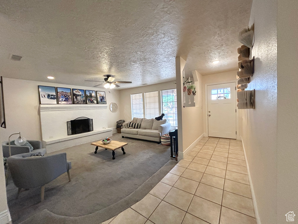 Living area with light tile patterned flooring, light colored carpet, a textured ceiling, a fireplace with raised hearth, and ceiling fan