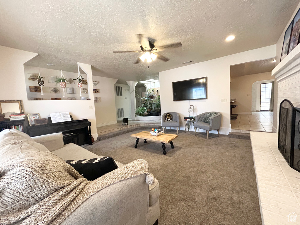 Living area featuring a textured ceiling, a ceiling fan, baseboards, a fireplace, and light carpet