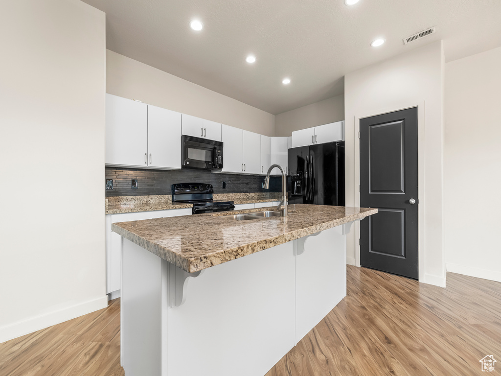 Kitchen with black appliances, decorative backsplash, a kitchen bar, a sink, and light wood-style flooring