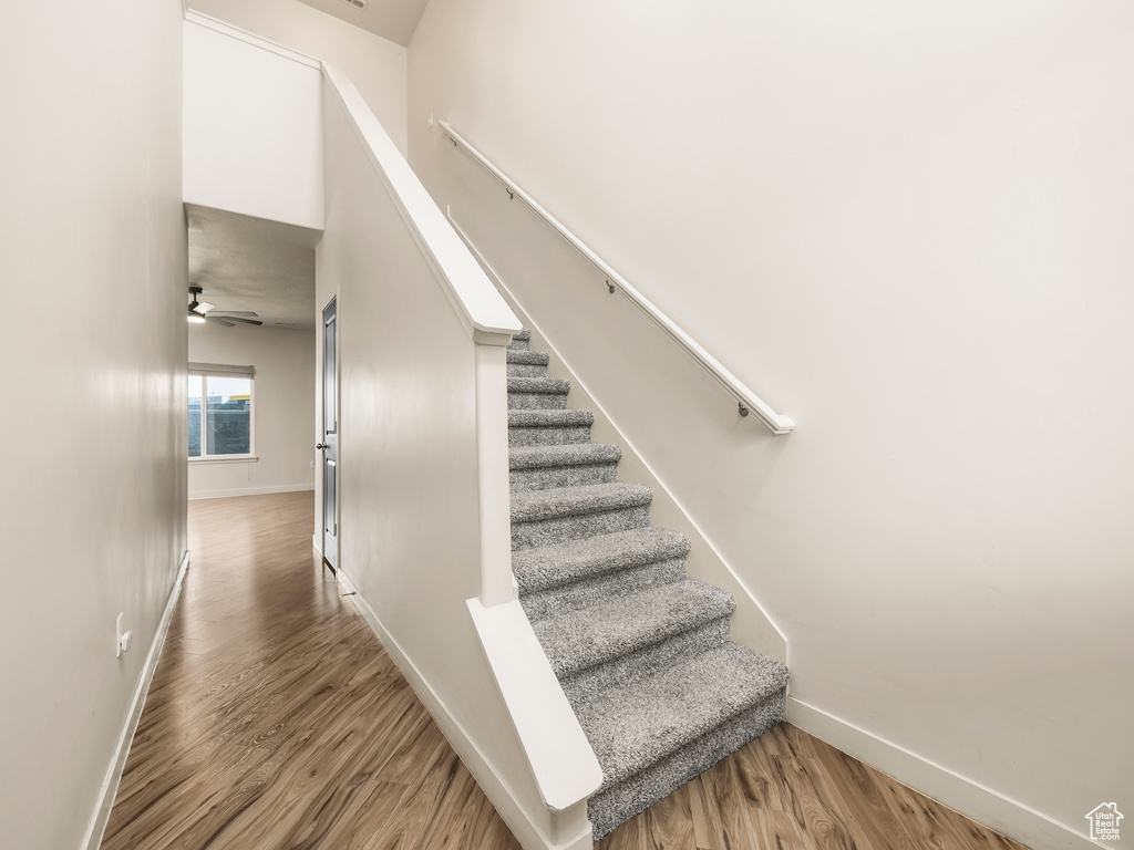 Stairway with baseboards, wood finished floors, and a ceiling fan