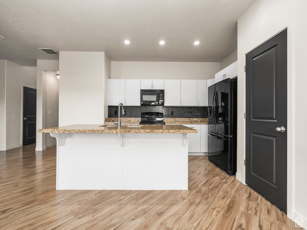 Kitchen featuring black appliances, a sink, a breakfast bar, light wood-type flooring, and recessed lighting