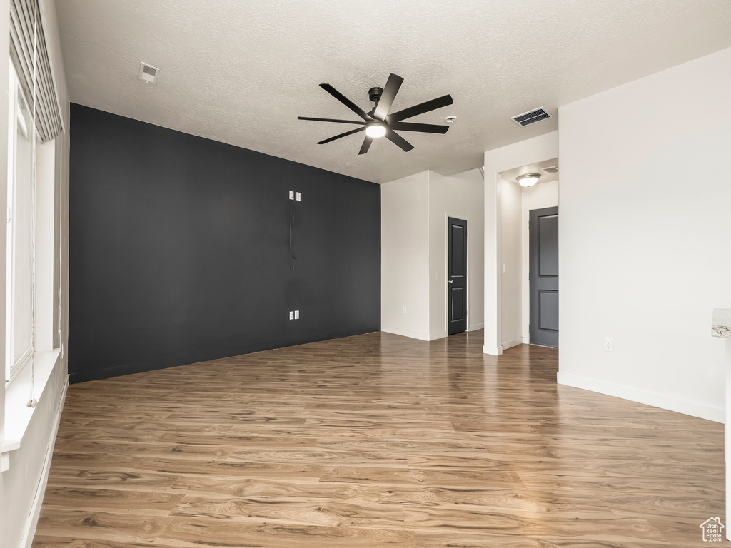 Unfurnished room with a ceiling fan, light wood finished floors, baseboards, and a textured ceiling