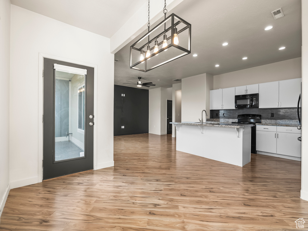 Kitchen featuring black microwave, a breakfast bar area, light wood-style floors, recessed lighting, and open floor plan