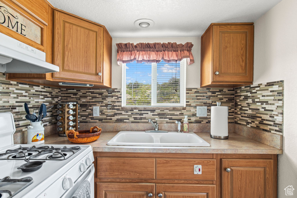 Kitchen with white range with gas cooktop, a sink, light countertops, and decorative backsplash