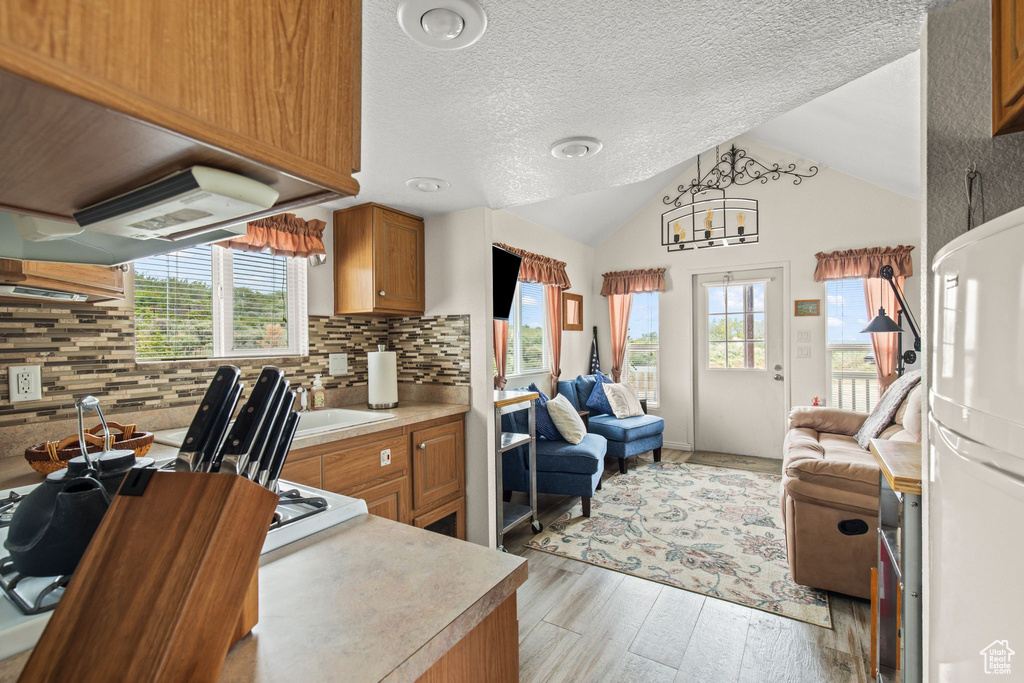 Kitchen with open floor plan, freestanding refrigerator, light wood finished floors, tasteful backsplash, and brown cabinetry