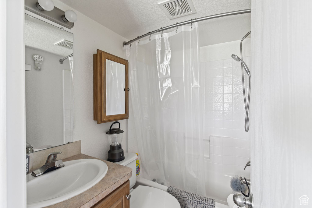 Bathroom featuring toilet, vanity, shower / bathtub combination with curtain, and a textured ceiling