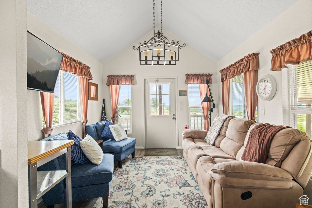 Living area featuring a chandelier, plenty of natural light, lofted ceiling, baseboards, and wood finished floors