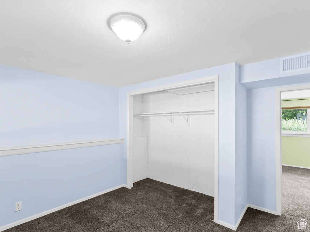 Unfurnished bedroom featuring dark colored carpet, a closet, and baseboards