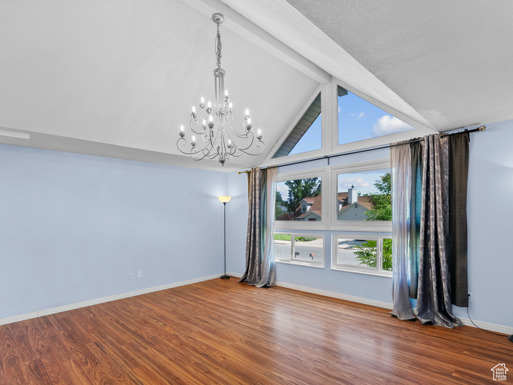 Empty room with a chandelier, wood finished floors, and baseboards