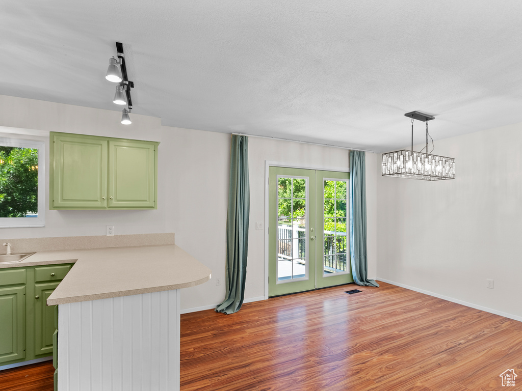 Kitchen with green cabinetry, a peninsula, light countertops, wood finished floors, and a sink