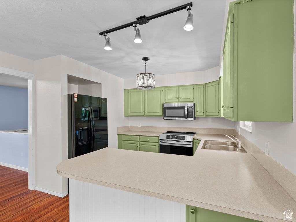 Kitchen featuring appliances with stainless steel finishes, a sink, green cabinets, a peninsula, and light countertops