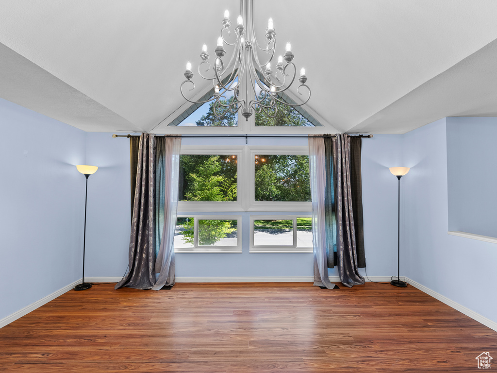 Spare room with healthy amount of natural light, a chandelier, lofted ceiling, wood finished floors, and baseboards