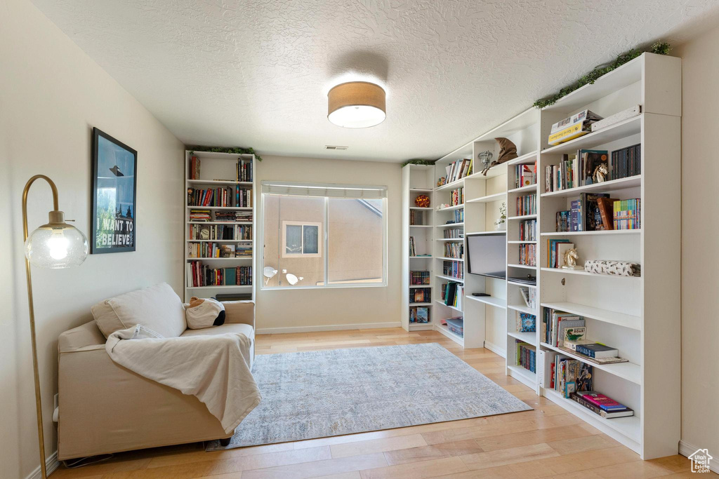 Sitting room with light wood-type flooring, a textured ceiling, and baseboards