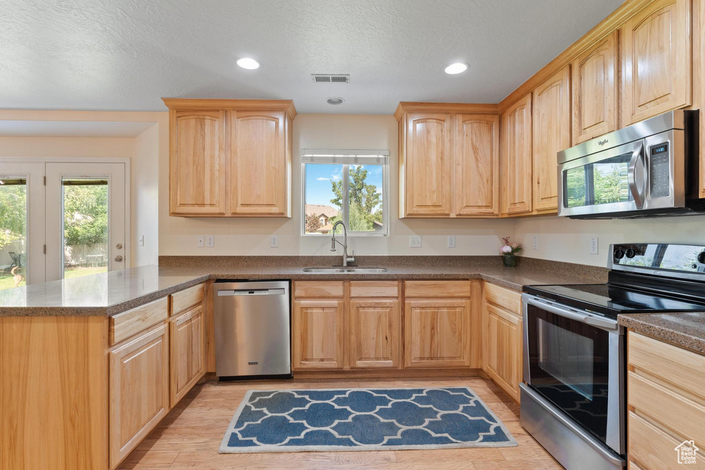 Kitchen with appliances with stainless steel finishes, light brown cabinets, a sink, a peninsula, and recessed lighting
