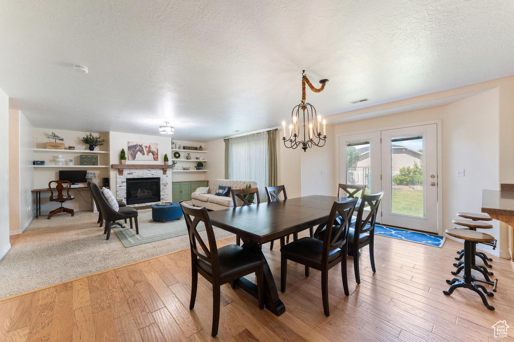Dining area with a textured ceiling, a fireplace, light wood-type flooring, built in features, and a chandelier