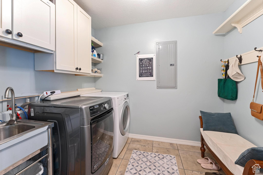 Laundry area featuring cabinet space, washing machine and clothes dryer, electric panel, baseboards, and light tile patterned flooring
