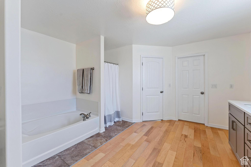 Full bathroom featuring vanity, a garden tub, wood finished floors, and baseboards