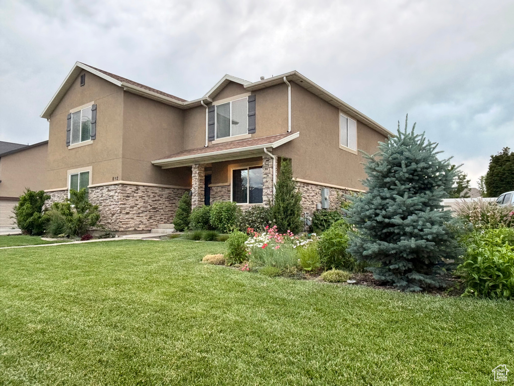 View of front of home featuring stucco siding, stone siding, and a front yard