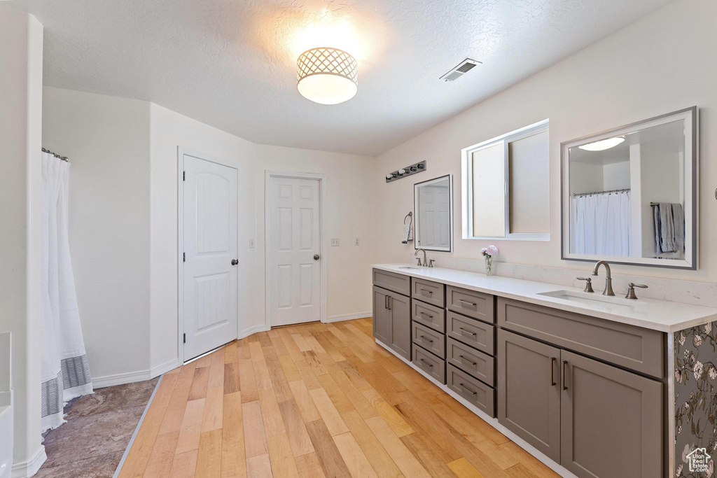Full bathroom with double vanity, wood finished floors, and baseboards
