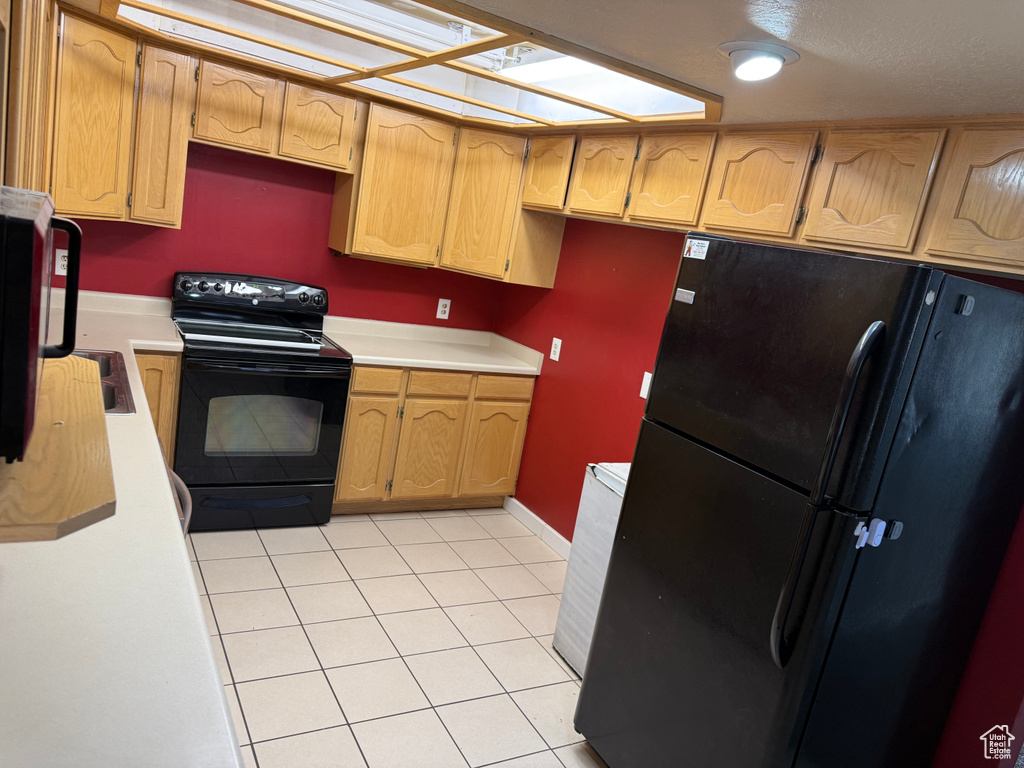 Kitchen with black appliances, light countertops, light tile patterned floors, and a skylight