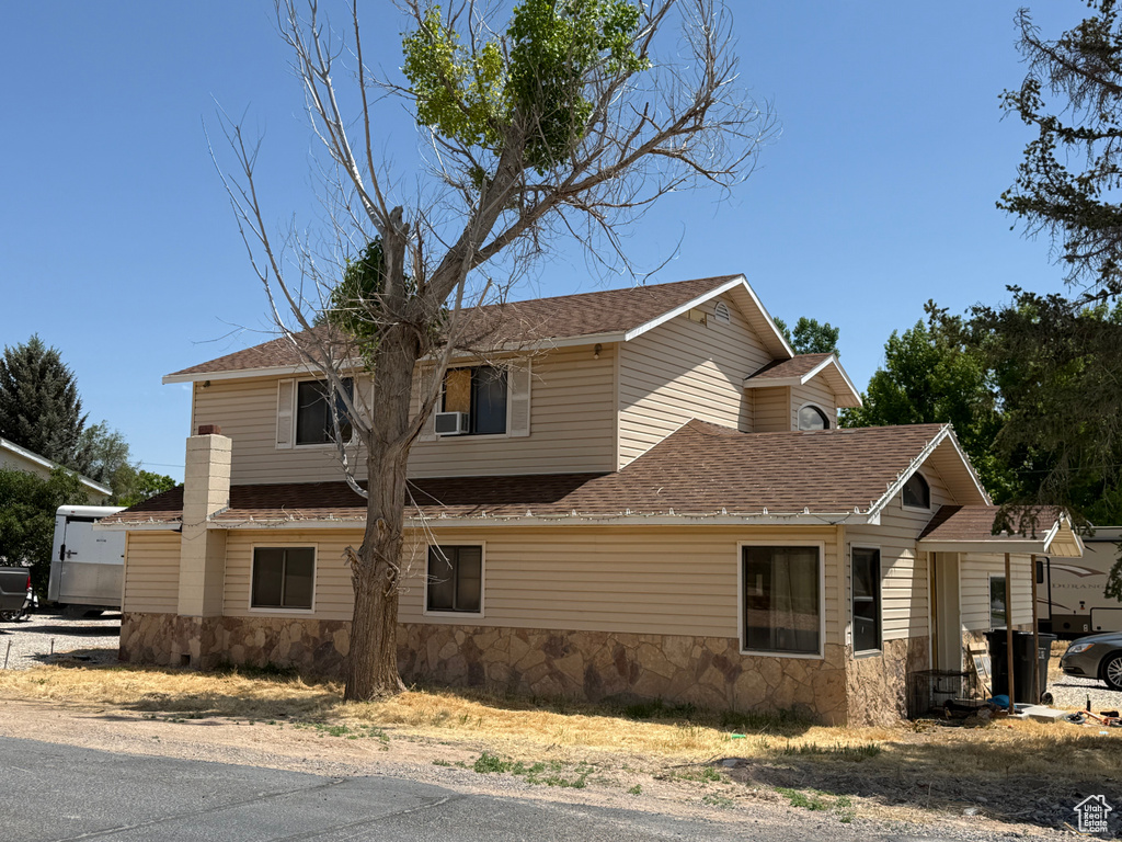 View of front of house featuring stone siding and roof with shingles