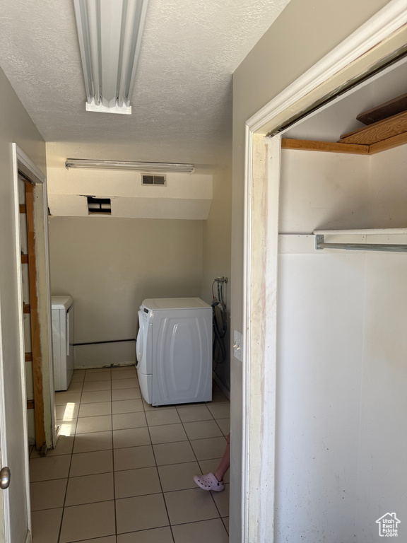 Laundry room featuring washer and dryer, light tile patterned flooring, and a textured ceiling