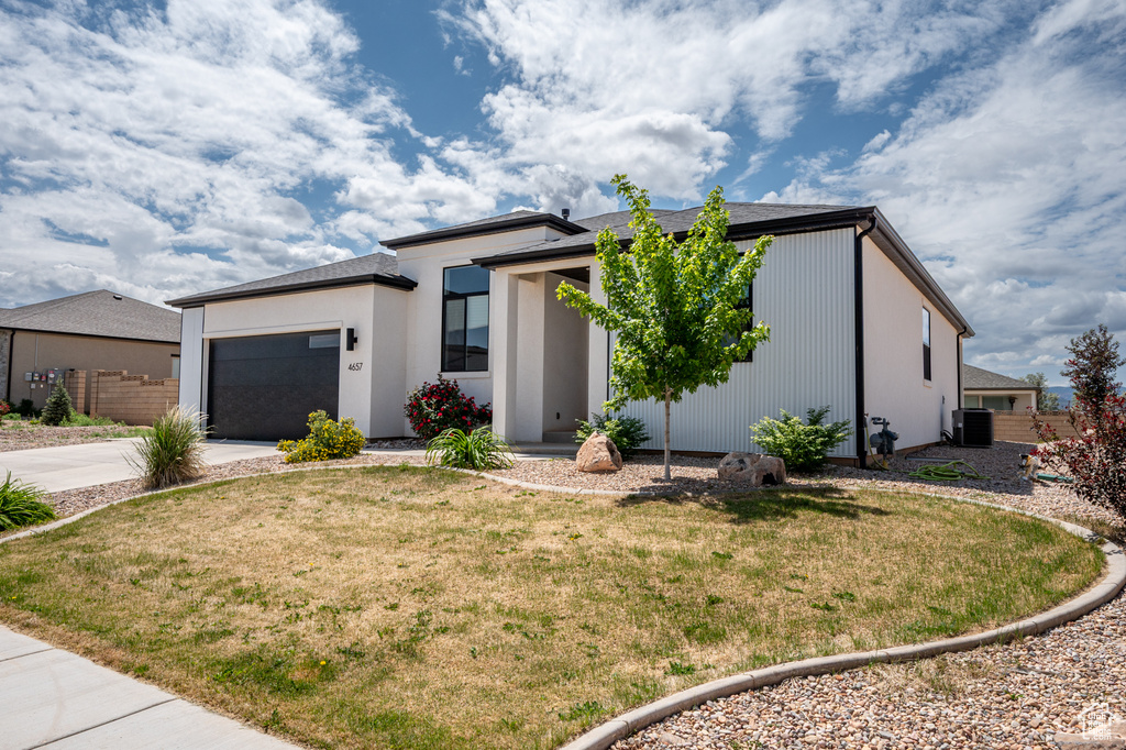 View of front of house featuring central air condition unit, concrete driveway, a garage, and a front lawn