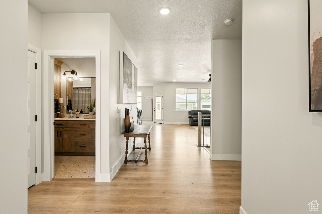 Hall with light wood finished floors, baseboards, a textured ceiling, a sink, and recessed lighting