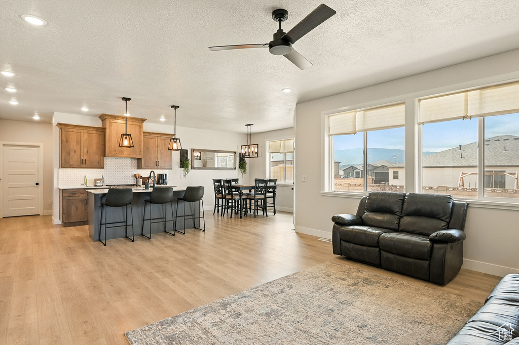 Living area featuring a ceiling fan, light wood-style floors, recessed lighting, baseboards, and a textured ceiling