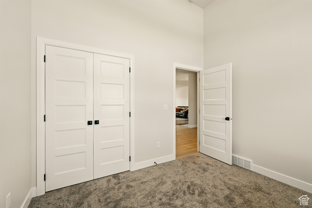 Unfurnished bedroom featuring carpet floors, baseboards, a towering ceiling, and a closet