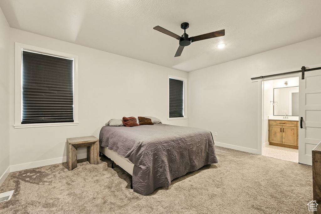 Bedroom featuring a barn door, baseboards, light colored carpet, and ensuite bath