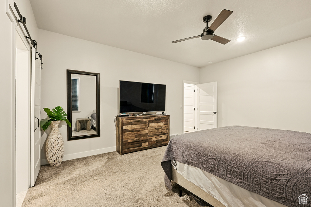 Carpeted bedroom featuring a barn door, baseboards, and ceiling fan