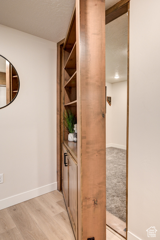 Hall featuring light wood-type flooring, a textured ceiling, and baseboards