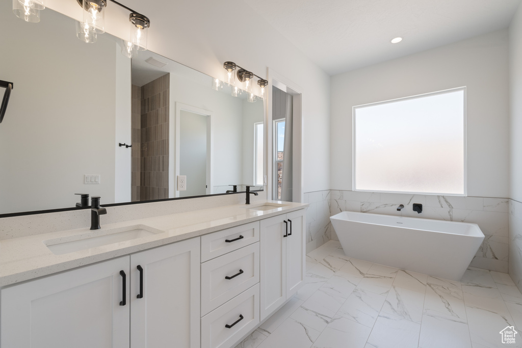 Full bathroom with double vanity, a soaking tub, marble finish flooring, recessed lighting, and wainscoting