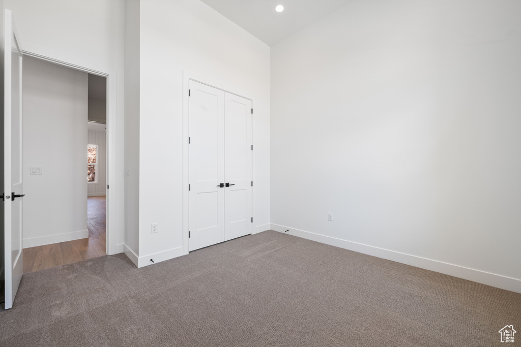 Unfurnished bedroom featuring carpet, baseboards, a closet, recessed lighting, and a towering ceiling
