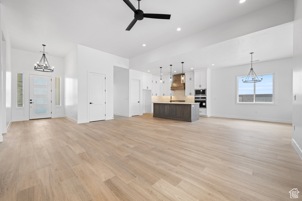 Unfurnished living room featuring a chandelier, baseboards, a ceiling fan, recessed lighting, and light wood-style floors