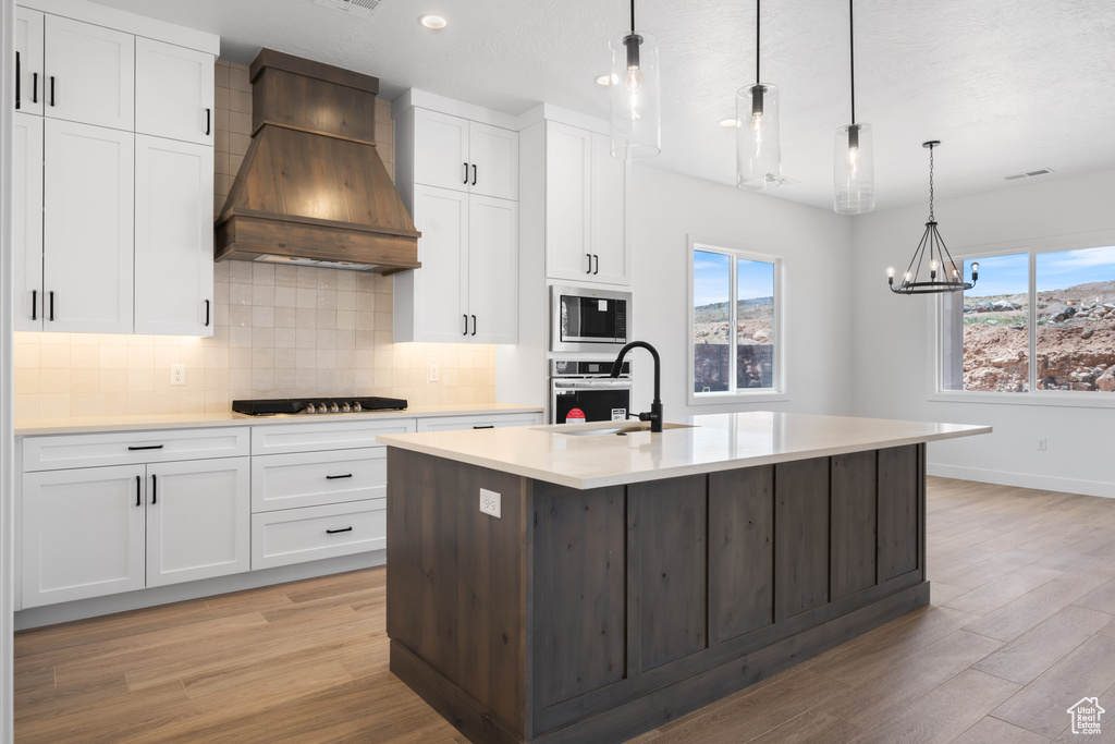 Kitchen with premium range hood, a sink, wall oven, light wood finished floors, and tasteful backsplash