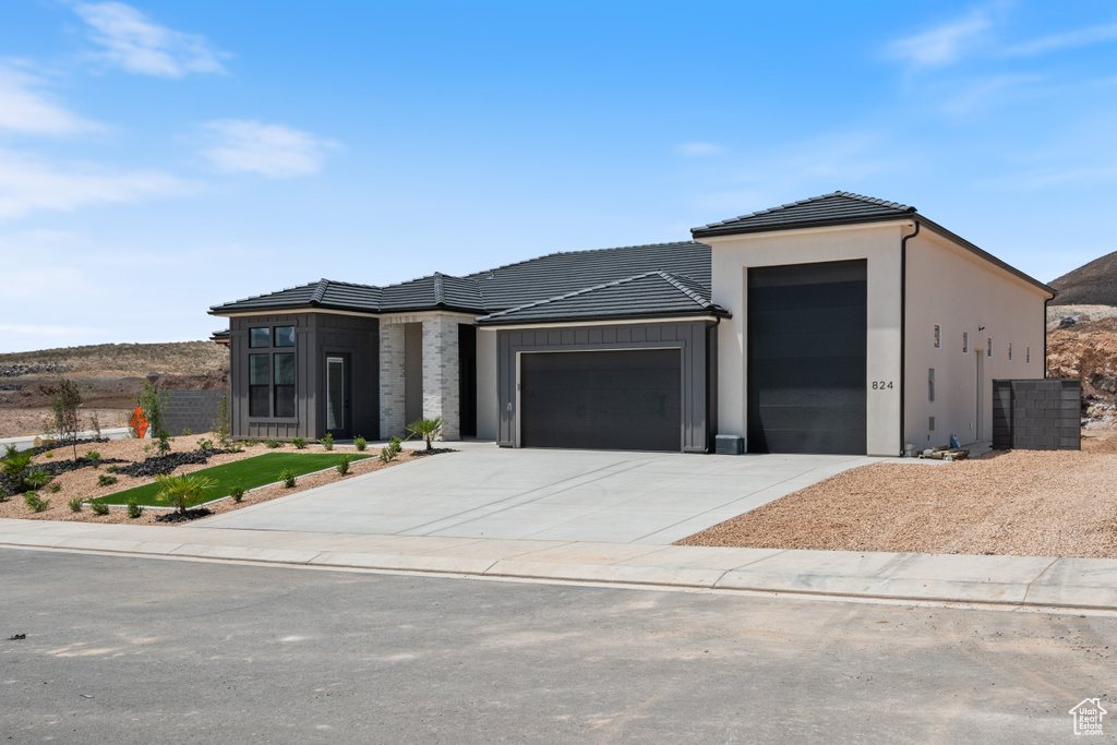View of front of property featuring a garage, driveway, a tile roof, board and batten siding, and stucco siding