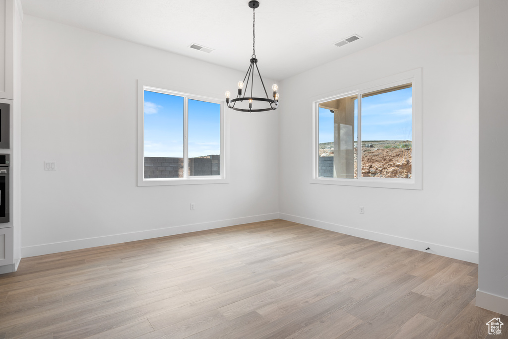 Spare room with a chandelier, plenty of natural light, light wood-style flooring, and baseboards