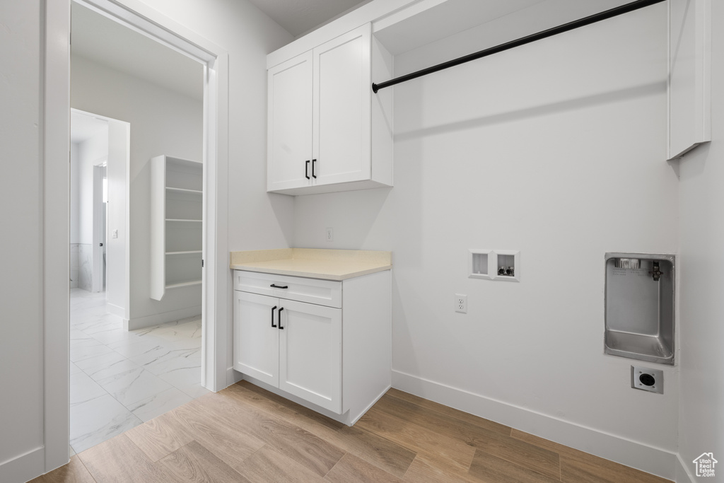 Laundry area with hookup for an electric dryer, hookup for a washing machine, cabinet space, baseboards, and light marble finish flooring