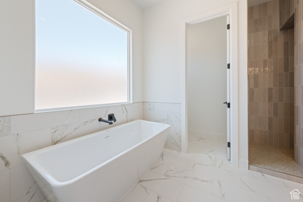 Full bath featuring tile walls, a soaking tub, tiled shower, marble finish floors, and wainscoting