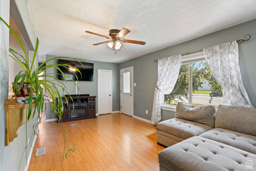 Living area with ceiling fan, baseboards, wood finished floors, and a textured ceiling