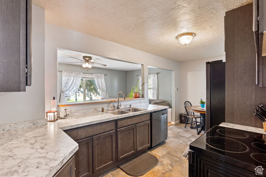 Kitchen featuring dishwashing machine, a sink, freestanding refrigerator, dark brown cabinetry, and a peninsula