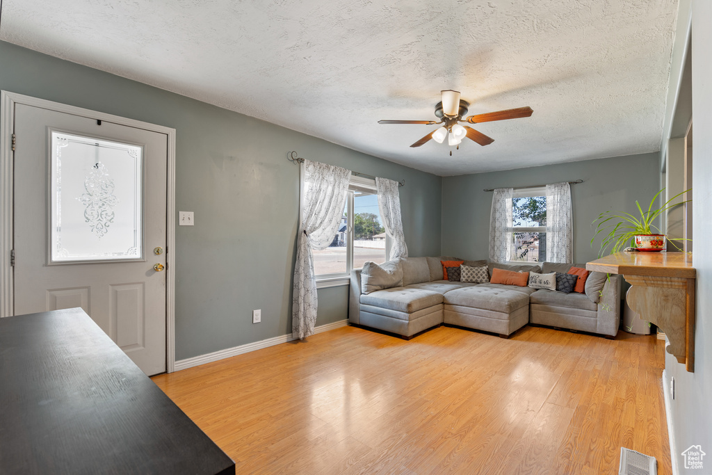 Living area with ceiling fan, plenty of natural light, light wood-type flooring, and a textured ceiling
