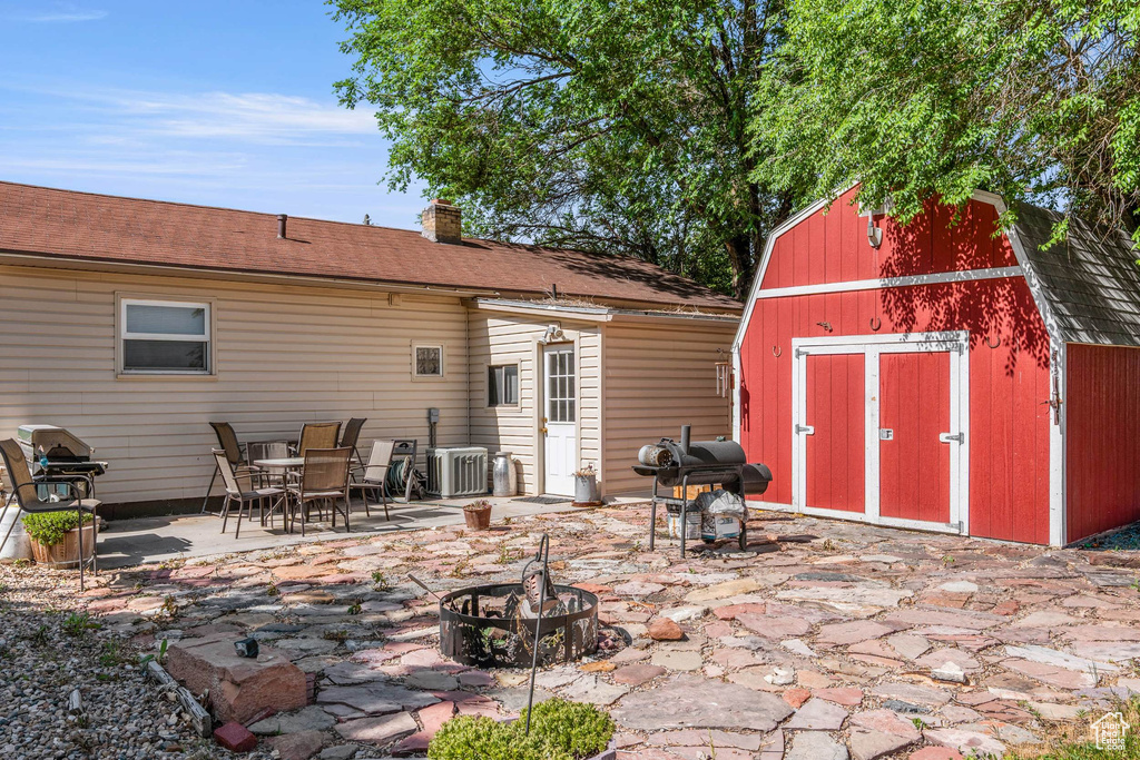 Back of property with an outdoor fire pit, central AC unit, a patio area, a chimney, and a gambrel roof